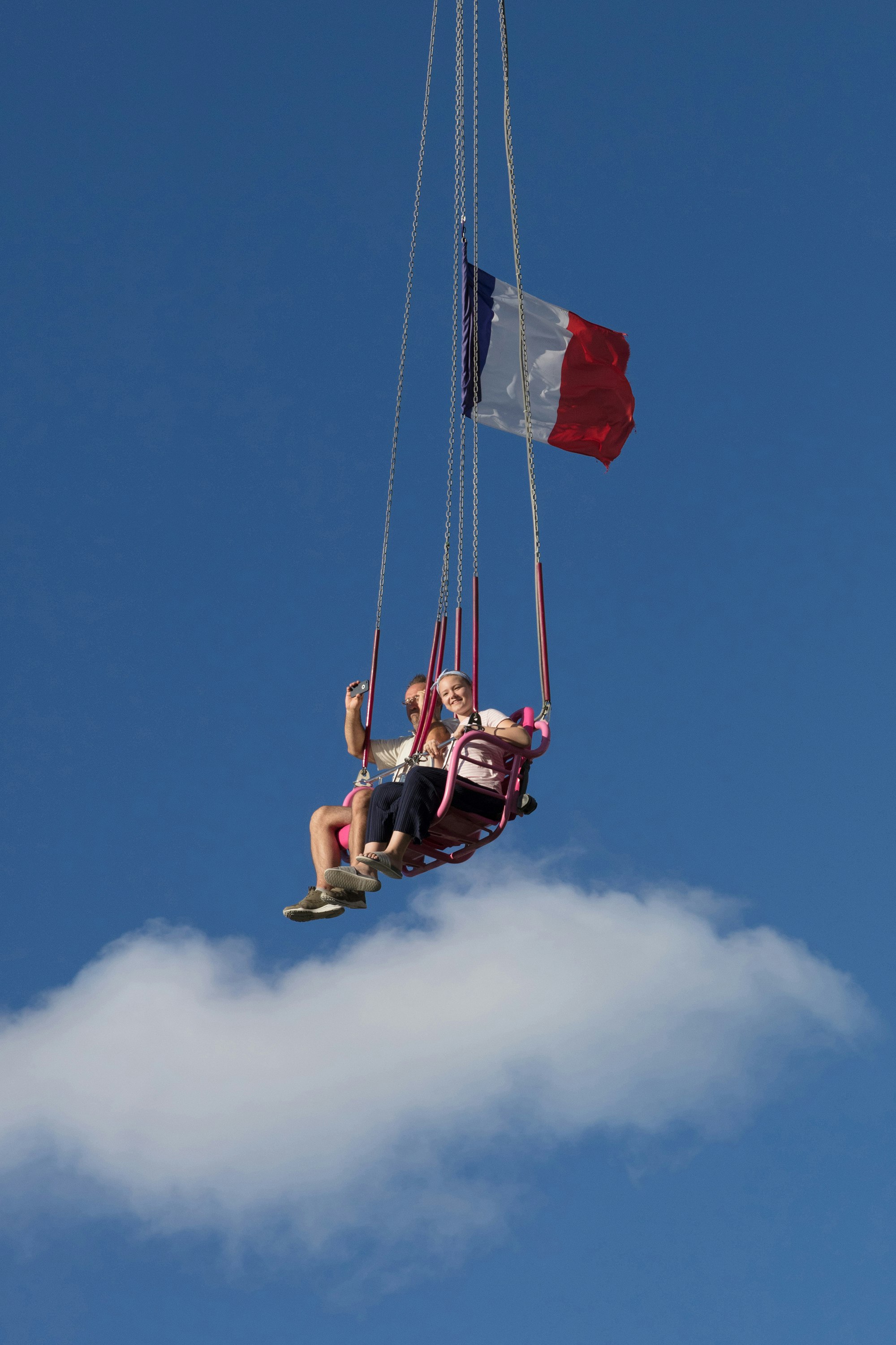 man in red shirt and black shorts riding on swing under blue sky during daytime